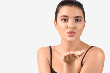 Young woman with beautiful lips blowing kiss on light background, closeup