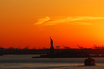 Silhouette of Statue of Liberty and Liberty Island in New York against an orange sunset sky.