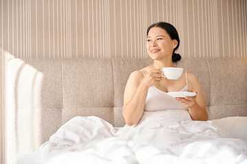 Obraz na płótnie Canvas Cheerful lady enjoying her morning drink in hotel room