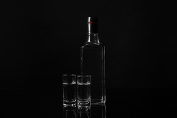 Shots and bottle of cold vodka on black background