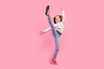 Full length photo of graceful girl wear stylish sweatshirt jeans raising leg up dancing look empty space isolated on pink color background