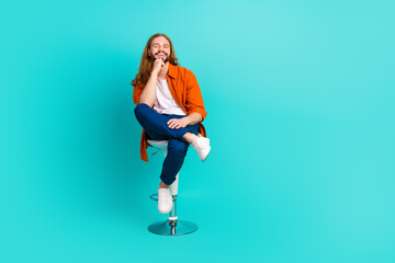 Fototapeta na wymiar Full size photo of positive guy with long hairdo sit on stool in barbershop get new haircut isolated on turquoise color background