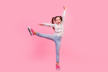 Full length photo of small girl wear stylish sweatshirt jeans raising leg up stand on tiptoe dancing isolated on pink color background