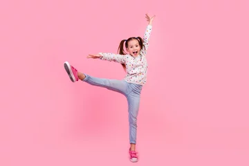 Foto op Canvas Full length photo of small girl wear stylish sweatshirt jeans raising leg up stand on tiptoe dancing isolated on pink color background © deagreez