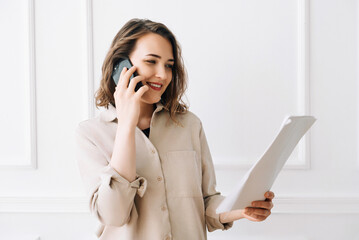 Smiling Millennial Woman Engaged in Phone Call, Discussing Documents with Client. Smiling...
