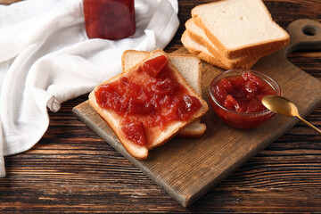 Board with delicious quince jam toasts on wooden background, closeup