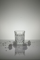 Vertical shot of crystal water glass, ice cubes and waterdrops around, on a white shiny surface