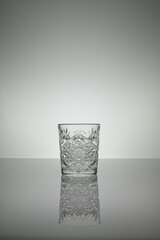 Crystal water glass reflecting on a gray surface with white background