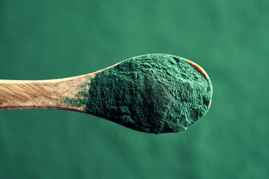 Green spirulina algae powder on a wooden spoon