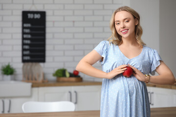 Young pregnant woman with apple in kitchen