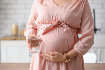 Young pregnant woman with glass of water in kitchen, closeup