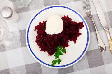 Portion of salad made of boiled and grated beetroot served on table with sour cream.