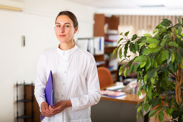 Portrait of a young confident female manager standing in the office with a folder of documents. Close-up portrait