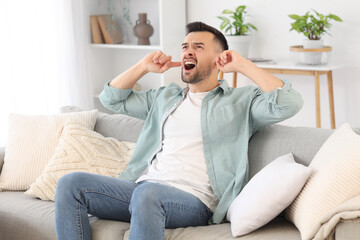 Young man covering ears because of loud neighbours at home - obrazy, fototapety, plakaty
