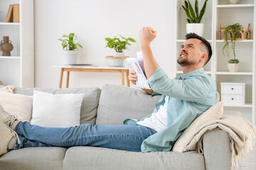 Young man with newspaper suffering from loud neighbours at home