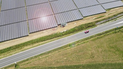 Obraz premium Red electric car with solar panel photovoltaic power plant during a sunny day. Rechargeable lithium battery zero emission alternative sustainable energy