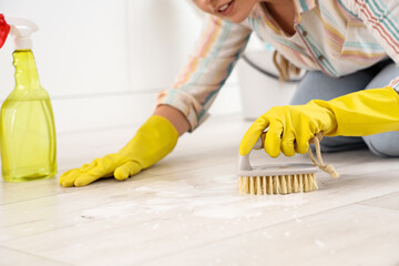 Female janitor cleaning floor with brush in kitchen, closeup