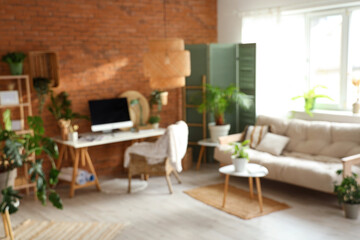 Blurred view of office with workplace, green plants and sofa