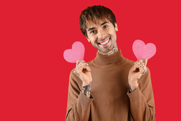 Handsome young man with paper hearts for Valentine's day on red background