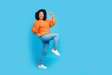 Fototapeta na wymiar Full length photo of lovely young lady raise fists win lottery lucky wear trendy knitwear orange garment isolated on blue color background