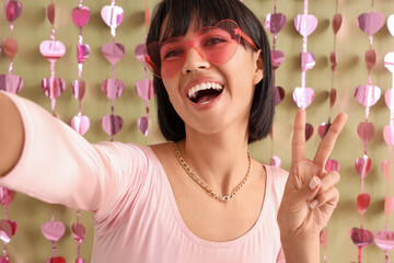 Obraz na płótnie Canvas Beautiful young woman in stylish sunglasses taking selfie on green background. Valentine's day celebration