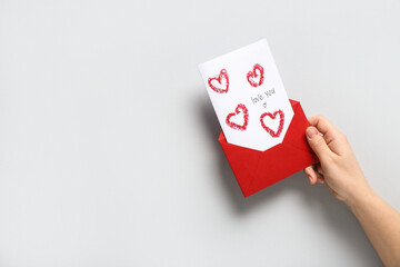Female hand with red envelope and greeting card on grey background, closeup. Valentine's Day...