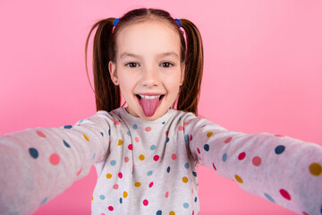 Photo of funky carefree small girl with ponytails wear stylish sweatshirt making selfie show tongue...
