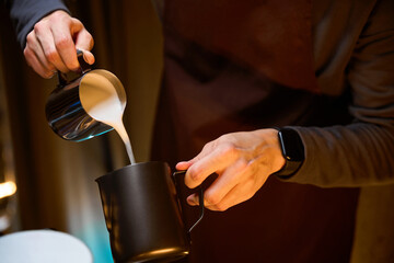 Barista pouring milk from pitcher preparing delicious coffee in coffee house