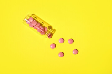 Overturned bottle with pills on yellow background