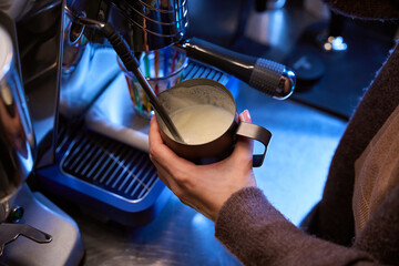 Unknown woman barista whisking milk for latte in steel jug