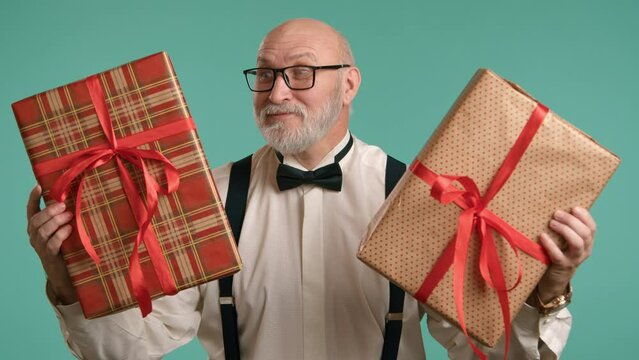 A festively dressed middle-aged man joyfully displays two gifts in beautiful boxes, offering to choose one of them. The man is in a shirt with a bow tie and suspenders, featuring baldness and a beard.