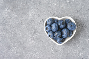 Fresh blueberries in a small heart-shaped bowl on gray concrete background with copy space. Organic...