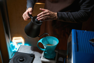 Barista pouring hot water over filter with ground coffee in the funnel