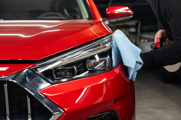 A man washes the headlights of a red car using a microfiber cloth and spray. 