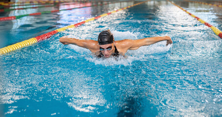 Front view of a powerful elite female swimmer competitor performing butterfly swim technique, arm...