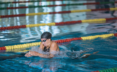 Female athlete swimming in breaststroke style in the pool lane, stroking, immersing, and lifting out of the water to breathe.