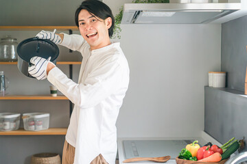 家のキッチンで料理をする鍋を持った日本人男性
