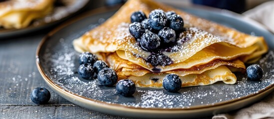 Blueberry crepes topped with powdered sugar on a small grey plate - obrazy, fototapety, plakaty