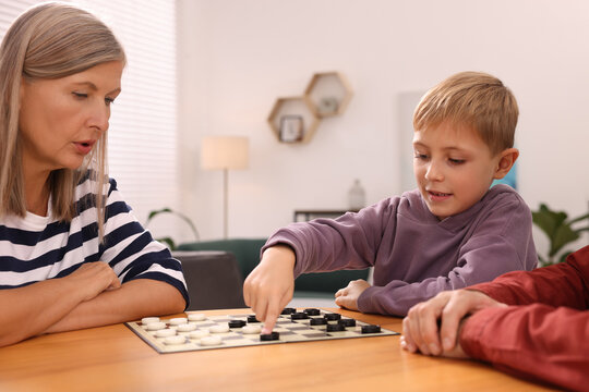 Family playing checkers at wooden table in room