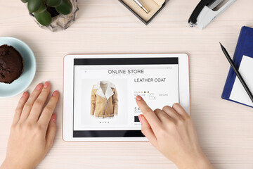 Woman with tablet shopping online at white wooden table, top view
