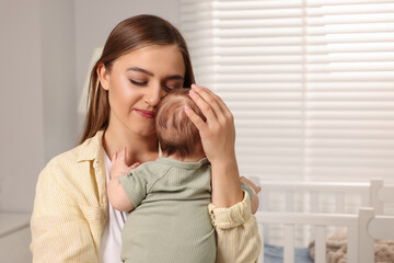 Mother holding her cute newborn baby in child's room, space for text