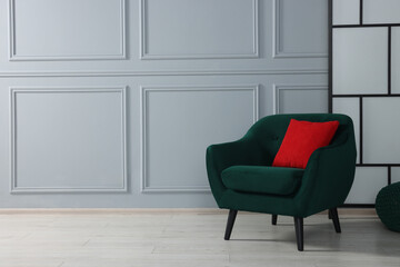Comfortable armchair with red pillow near light grey wall indoors. Space for text