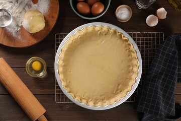 Pie tin with fresh dough, rolling pin and ingredients on wooden table, flat lay. Making quiche