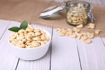 Tasty cashew nuts and green leaves on white wooden table, closeup