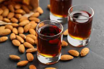 Glasses with tasty amaretto liqueur and almonds on dark gray table, closeup