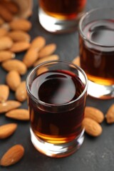 Glasses with tasty amaretto liqueur and almonds on dark gray table, closeup