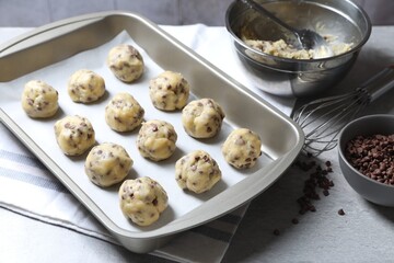 Baking pan with raw chocolate chip cookie balls on table