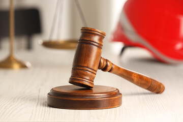 Law concept. Gavel, scales and red hard hat on white wooden table, closeup