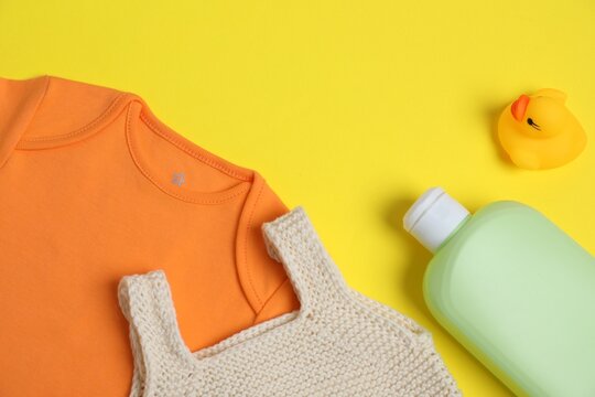 Bottles of laundry detergents, baby clothes and rubber duck on yellow background, flat lay. Space for text