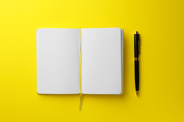 Open notebook with blank pages and pen on yellow background, top view. Space for text